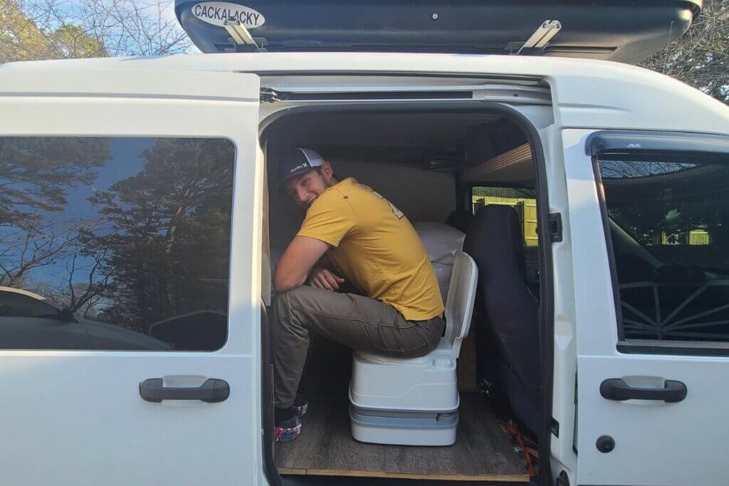 him sitting on a camper van chemical toilet in a van