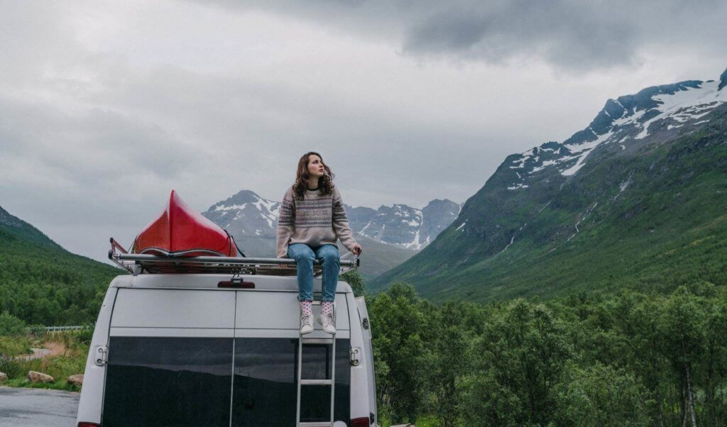 a girl on top of a camper van trying to stay warm in the winter time.