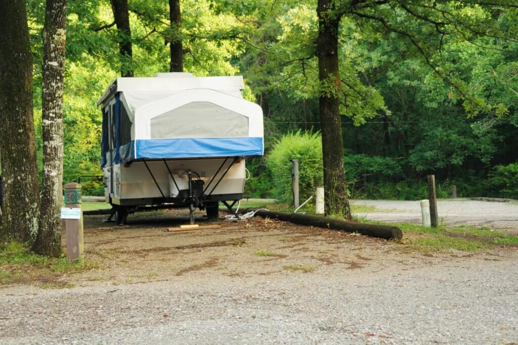 pop up camper in a spot at a camp ground. has blue lining on the tent part.