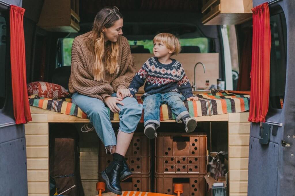 mom and son sitting in back of camper van with doors open wearing winter clothes