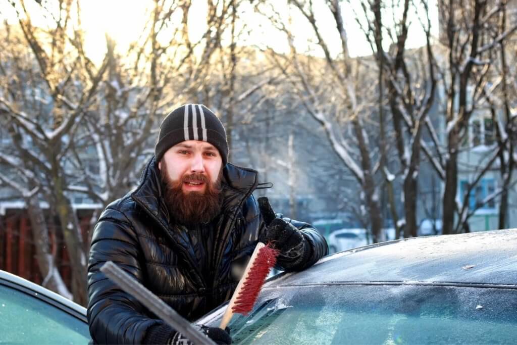 man brushing snow off of vehicle