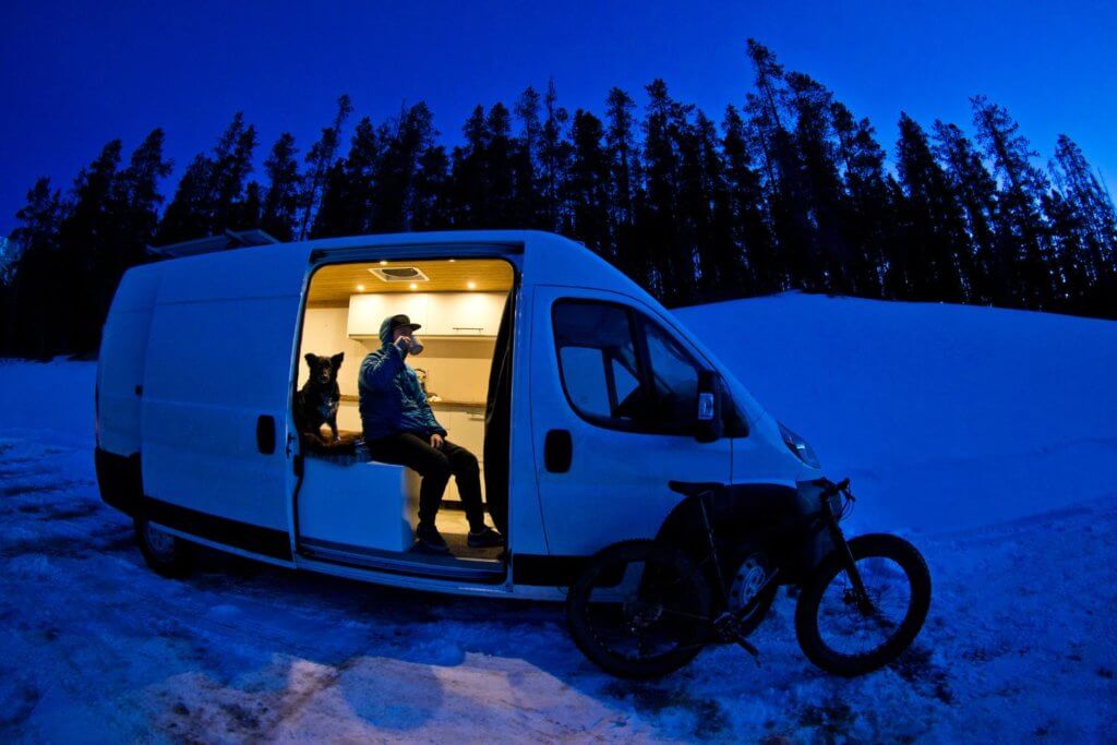 man and dog sitting inside a camper van in the snow.