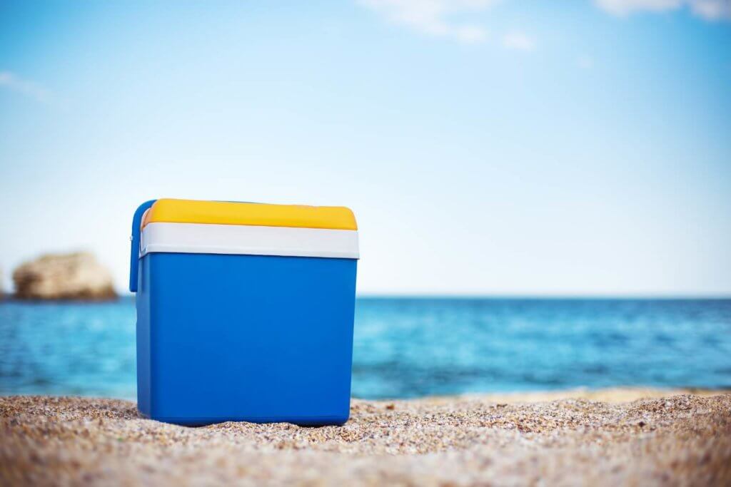 blue cooler in the sand, yellow top with white outlines