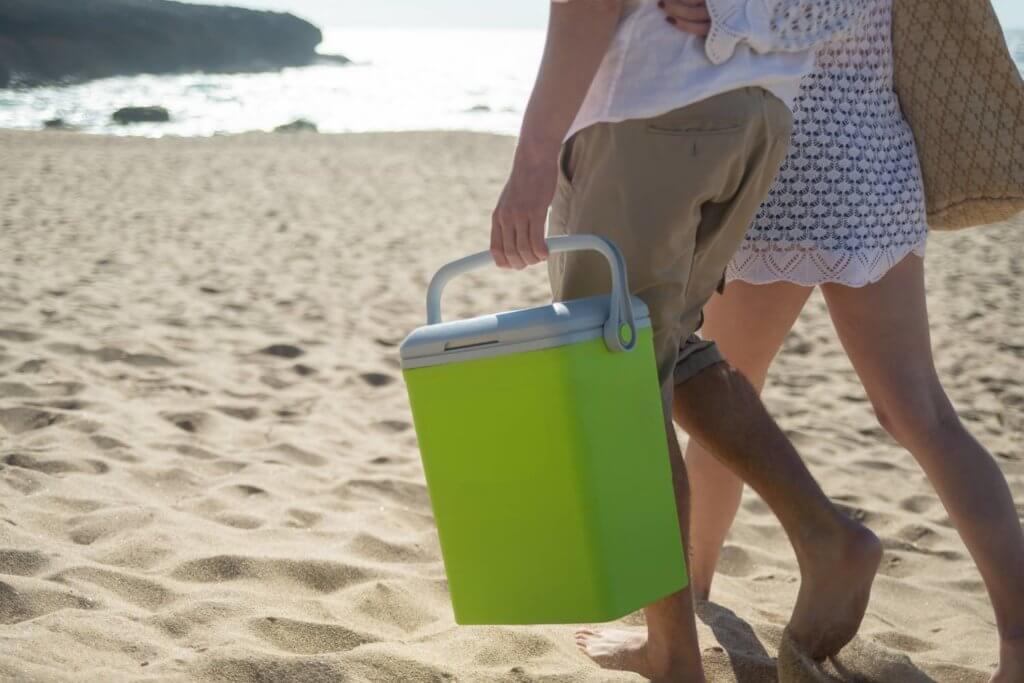 a couple holding a camper van cooler on the beach