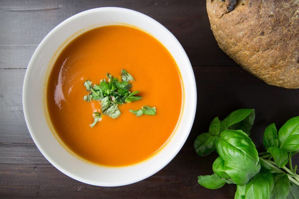 Fall time foods, orange looking soup with basil leaves and a loaf of bread