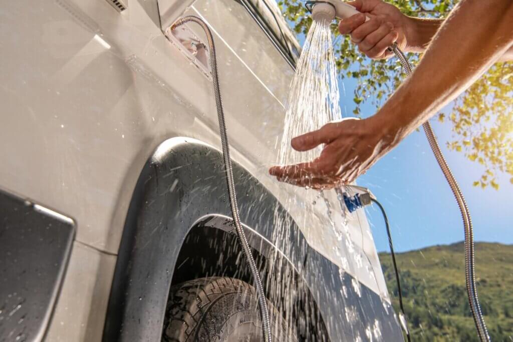 man holding shower head outside of a camper van
